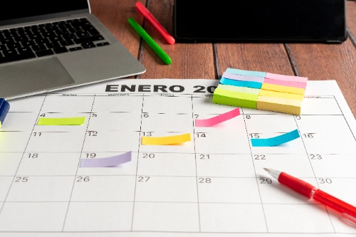 Calendario mensual con notas adhesivas de colores marcando fechas importantes